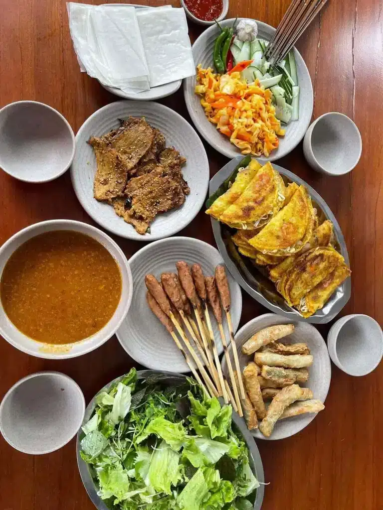 Table de bánh xèo, brochettes et galettes de riz, exemple de ce que manger au Vietnam dans un restaurant local